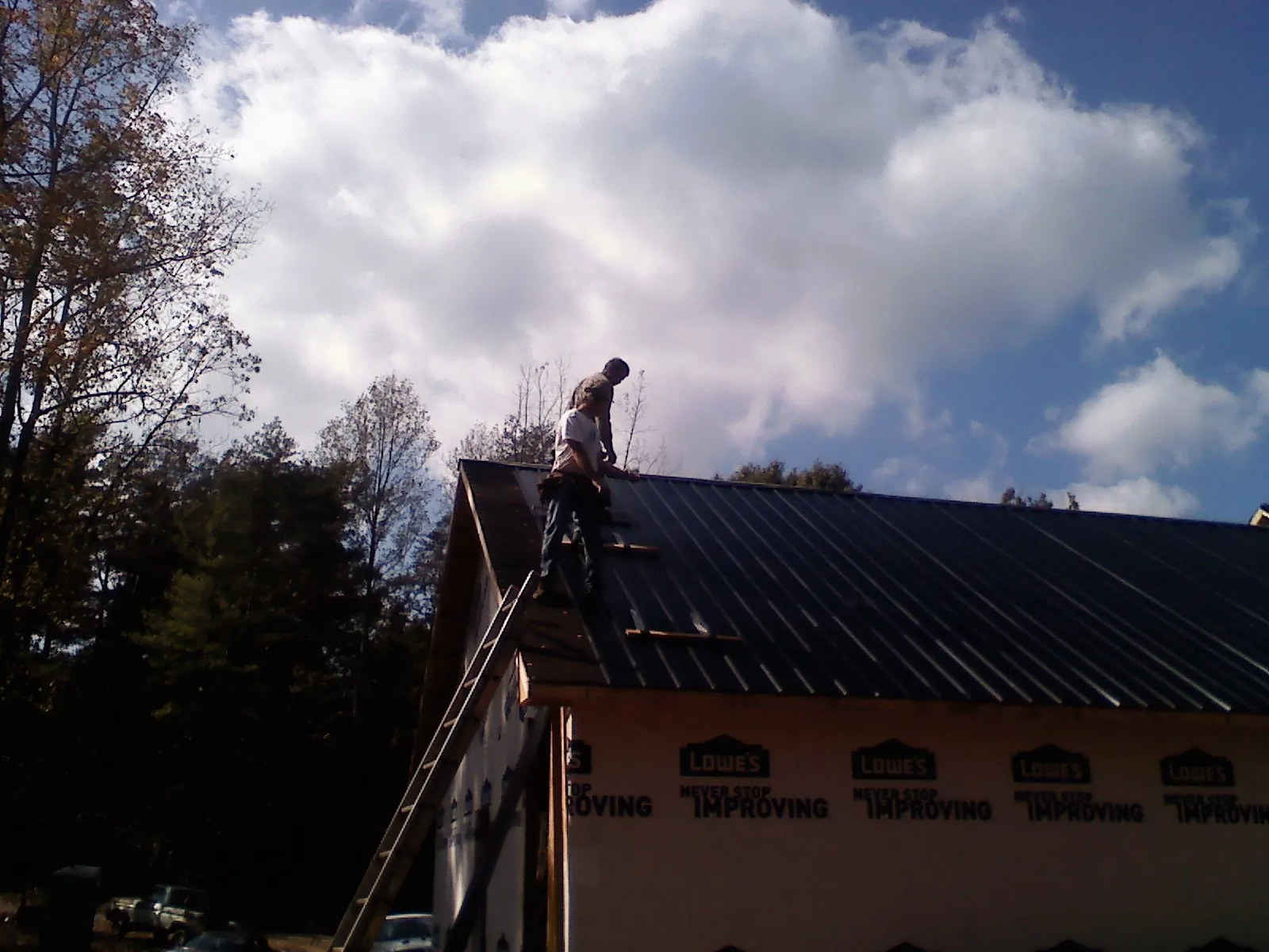 Roofer fastening dark metal panels high against a cloudy sky, from a Roof Inspection job in Mount Union