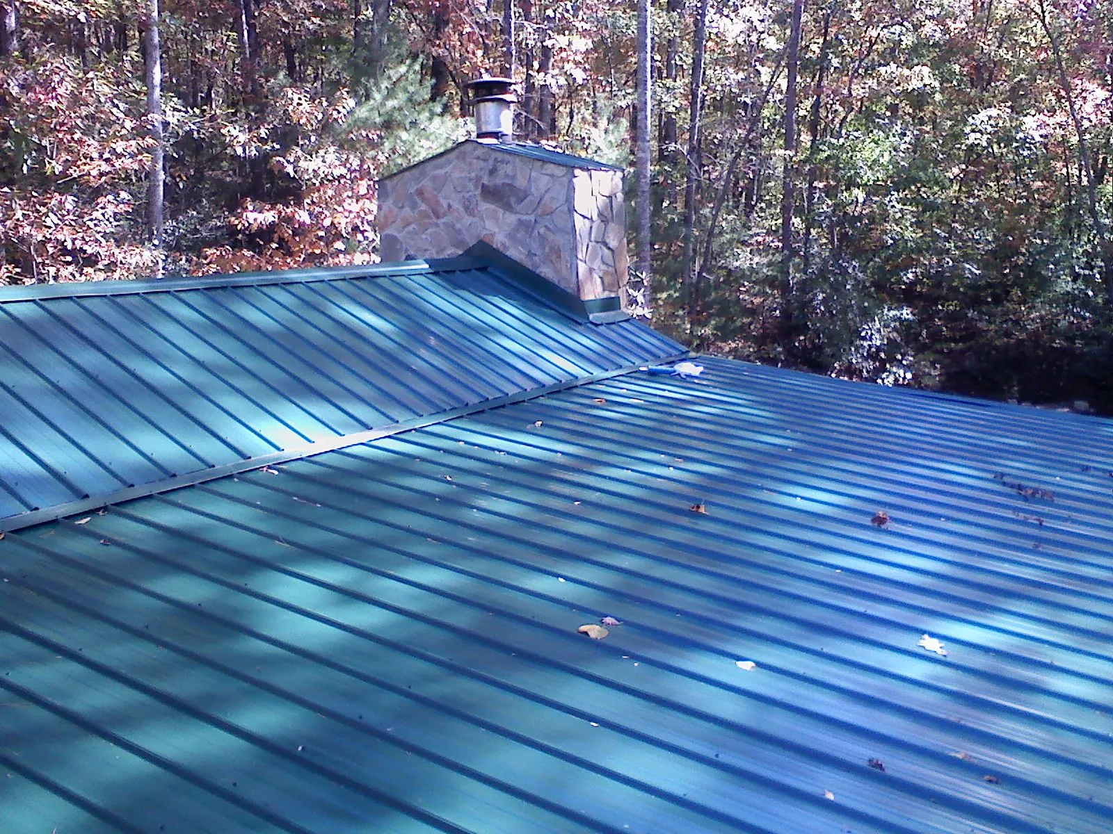 New green metal roof and stone chimney surrounded by autumn woods in Mount Union