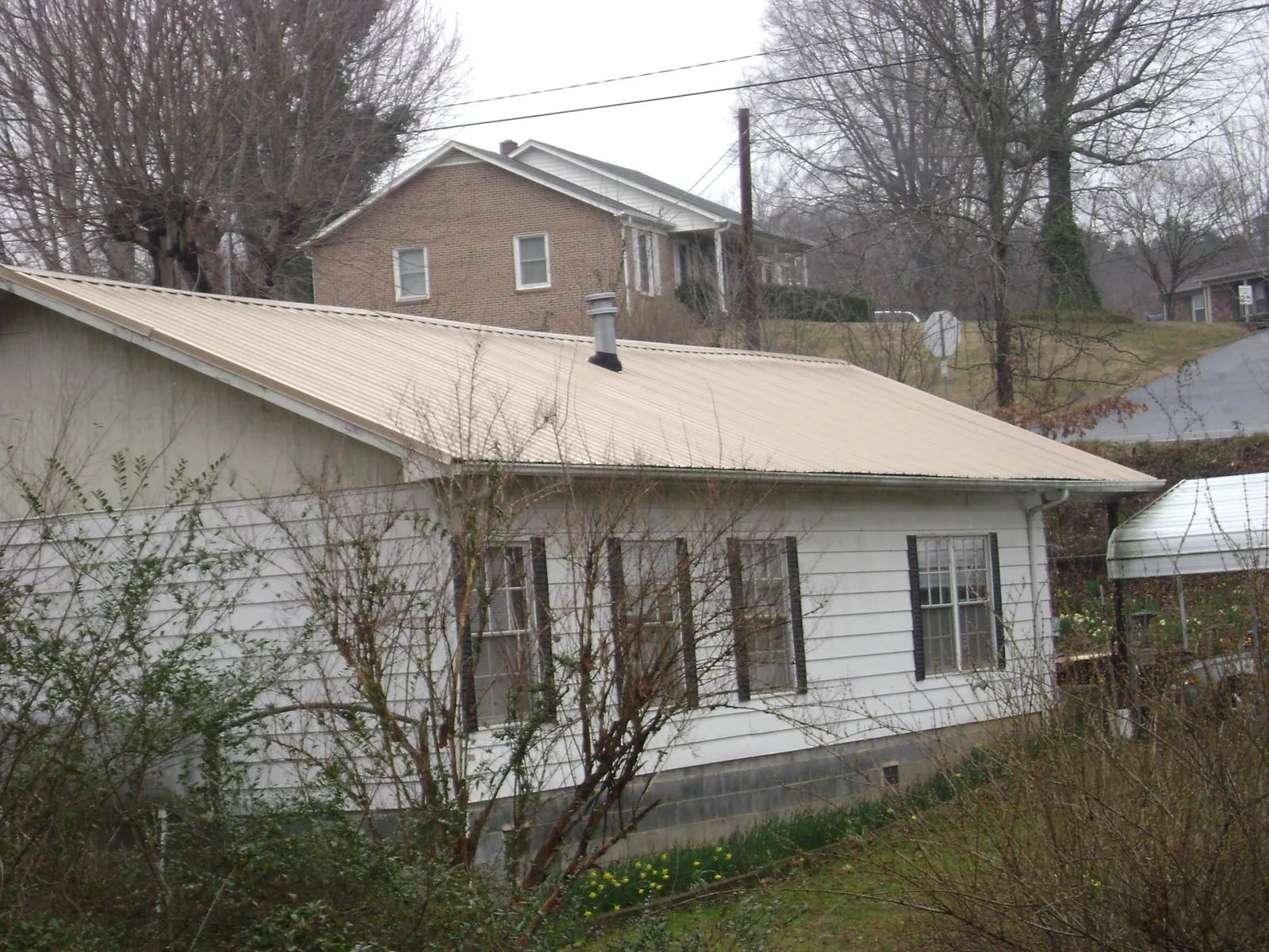 Tan metal roof on a white sided house set into a hillside — Commercial Roofing by Roofing Brothers in Mount Union